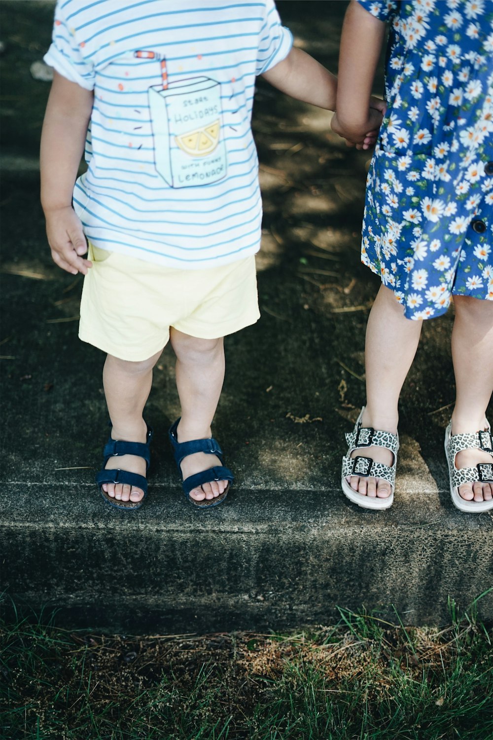 two children holding hands while standing on concrete pavement