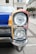 A close-up view of a vintage car's headlight and front corner. The vehicle features a colorful design with sections of red, yellow, and blue. The chrome and glass of the headlight are highly reflective, and the surrounding architecture of the street creates a classic urban backdrop.