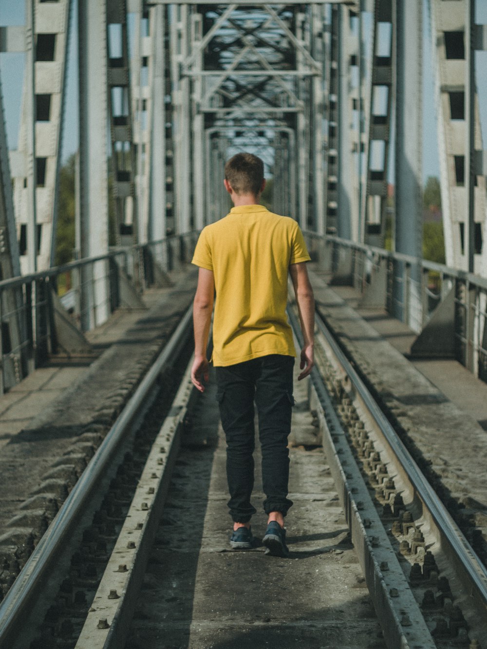 man wearing yellow polo shirt walking on train rails