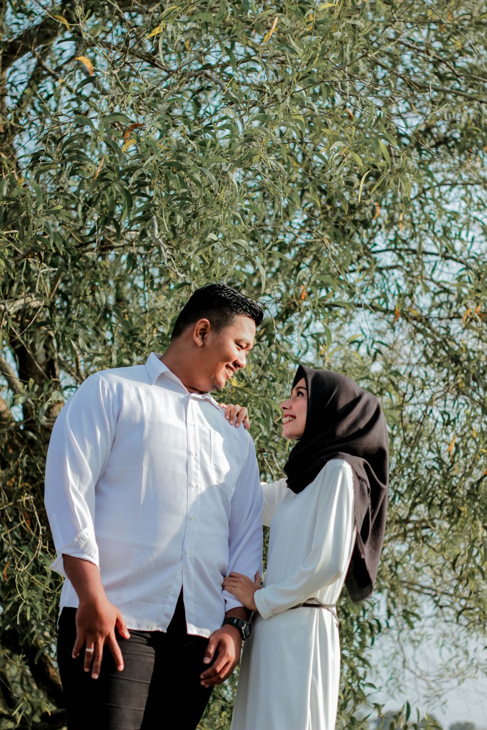 smiling man and woman stand beside tree