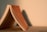 A paperback book is partially open, resting on a surface. The pages are slightly curved, creating a triangular shape, and the warm lighting casts soft shadows on the background.