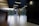 A modern interior space with a sleek design featuring tiled flooring and wood paneling. Large glass doors at the end of the corridor offer a view of a neatly maintained garden with green foliage. The ceiling has inset lighting that casts a soft glow.