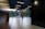 A modern interior space with a sleek design featuring tiled flooring and wood paneling. Large glass doors at the end of the corridor offer a view of a neatly maintained garden with green foliage. The ceiling has inset lighting that casts a soft glow.
