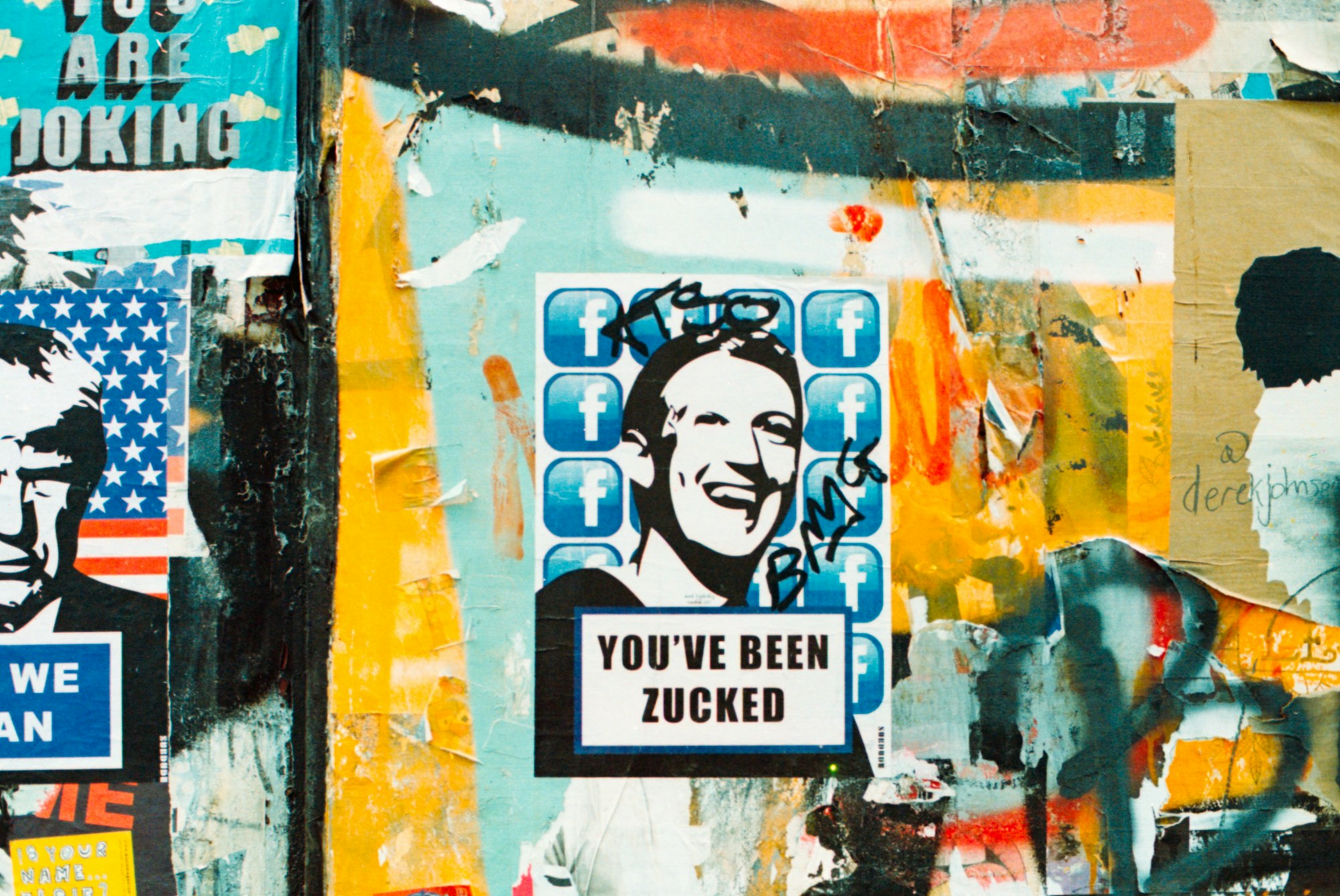 A wall of graffiti art and posters, the center one showing a picture of Mark Zuckerberg with text saying "You've been zucked."