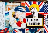 A collage of street art featuring satirical political imagery. The central focus includes a depiction of a child-like character with an elongated nose and blue paint dripping over the face, juxtaposed with another stylized image of a person's face with yellow hair above a sign that reads 'BLOND AMBITION'. The background includes various elements resembling the Union Jack flag.