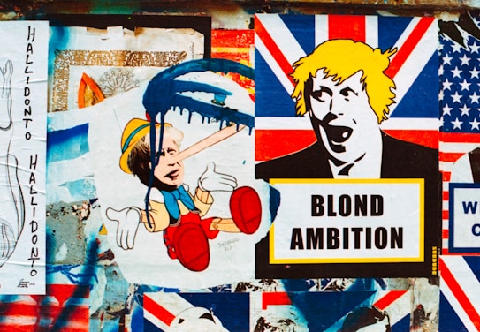 A collage of street art featuring satirical political imagery. The central focus includes a depiction of a child-like character with an elongated nose and blue paint dripping over the face, juxtaposed with another stylized image of a person's face with yellow hair above a sign that reads 'BLOND AMBITION'. The background includes various elements resembling the Union Jack flag.