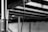 A silver microphone with a black grille is suspended by a cord in an industrial setting, with blurred beams and a brick wall in the background.