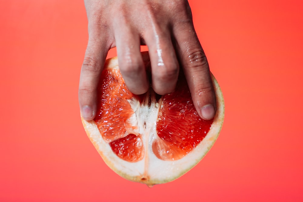 personne tenant un fruit de pomelo rouge