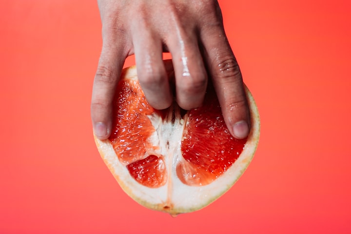 A photo of a hand with two fingers inserted in an orange. The orange is used to mimick the vagina