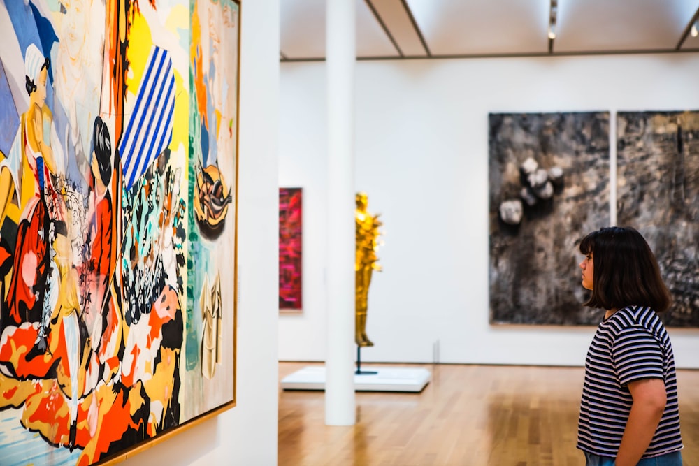 woman standing and facing a painting on wall inside gallery