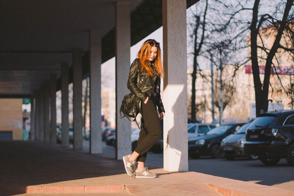 woman standing beside building pillar near parked cars