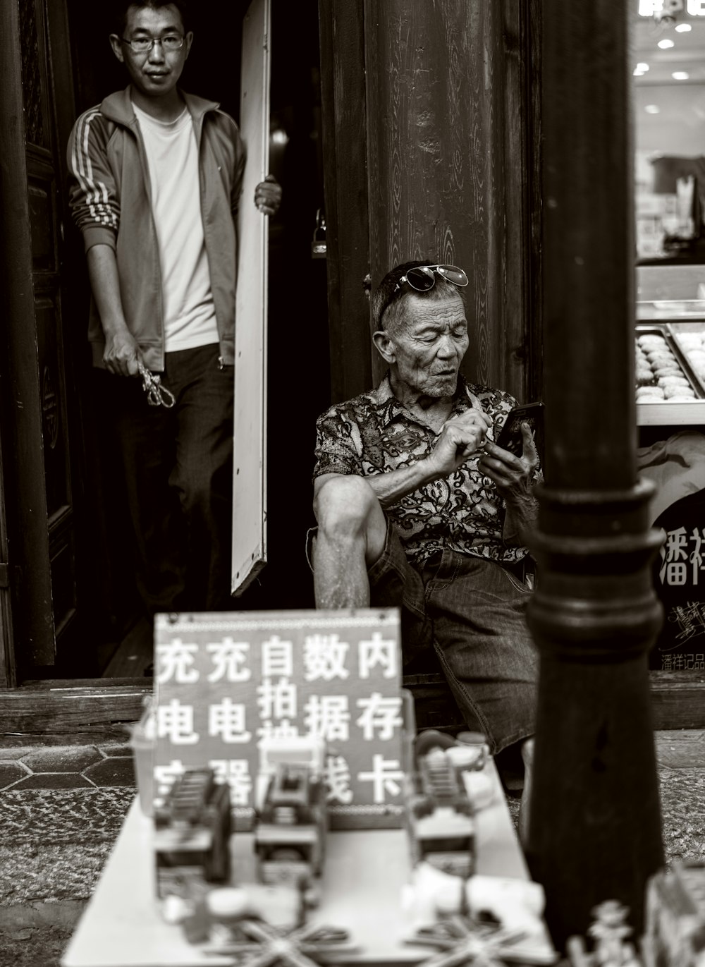 grayscale photo of man sitting on stairs while using smartphone