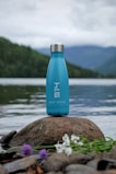 A portable water purifier bottle being used outdoors at a picnic near a lake.