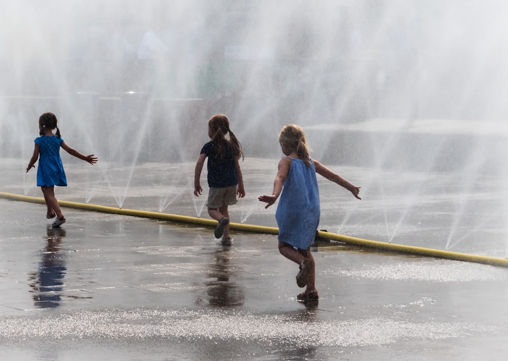 three girls running beside water fountains