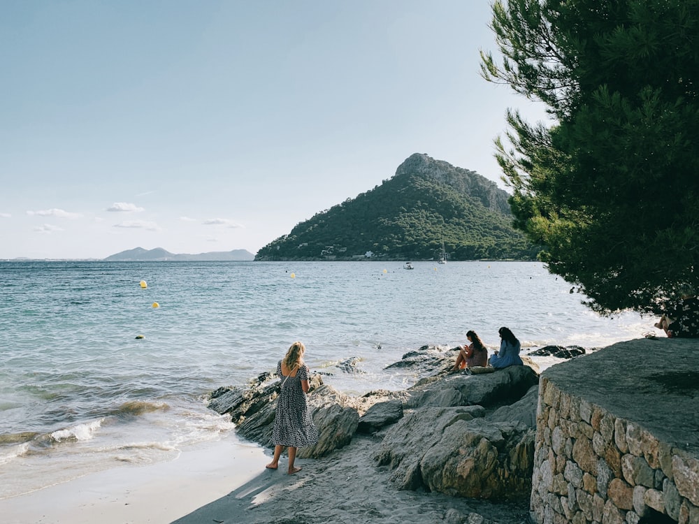 three women siting on rock formation near sea