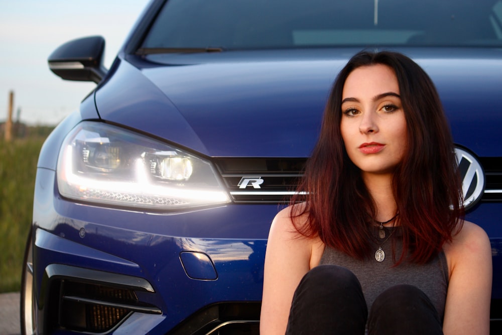 a woman sitting in front of a blue car
