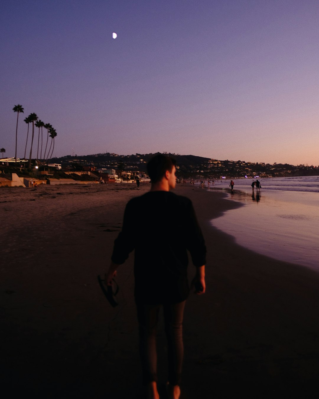 man walking along black sand beach shore