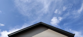 A rooftop with beige siding and a dark gray edge against a bright blue sky with scattered clouds.