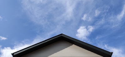 A rooftop with beige siding and a dark gray edge against a bright blue sky with scattered clouds.
