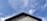 A rooftop with beige siding and a dark gray edge against a bright blue sky with scattered clouds.