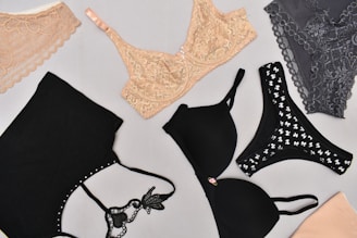 Various types of lingerie are displayed on a light gray background, including lace bras and bralettes in nude and gray, along with black bras featuring different designs.
