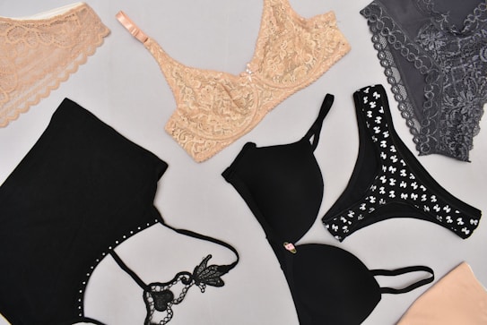 Various types of lingerie are displayed on a light gray background, including lace bras and bralettes in nude and gray, along with black bras featuring different designs.