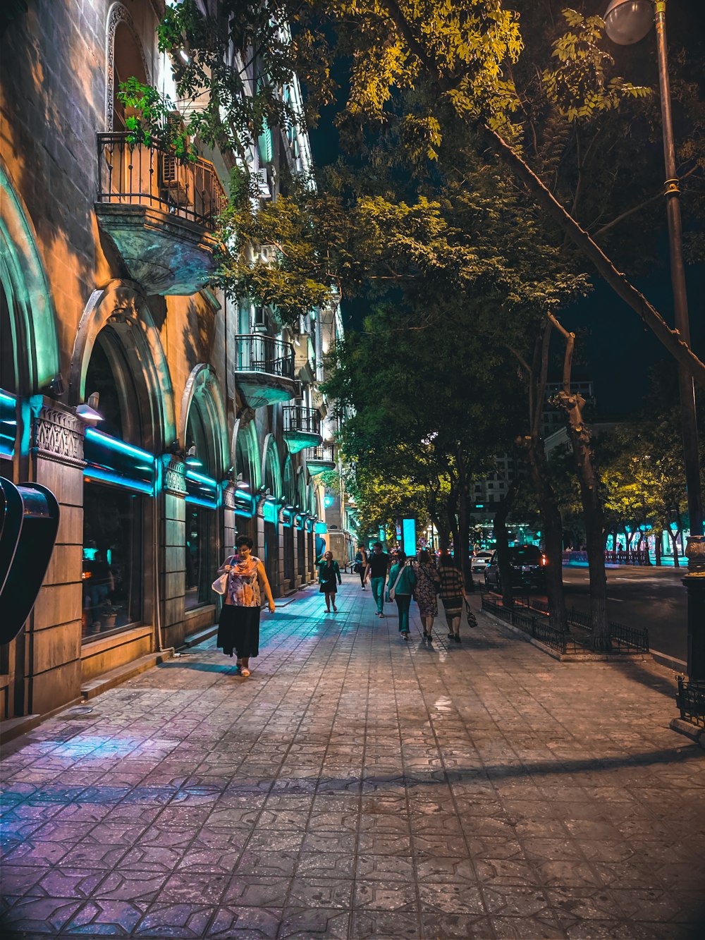 photo of woman wearing beige floral top and black skirt walking on street during nighttime