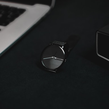 A sleek steel watch resting on a wooden table next to a neatly wrapped gift box.