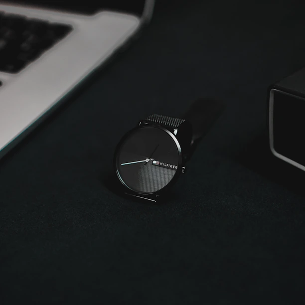 A stylish wristwatch resting on a sleek leather wallet, both set against a minimalist white surface.
