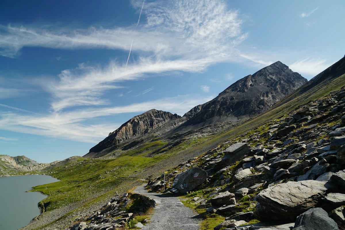 A rocky path beside a lake on the Gemmi pass above Leukerbad, under grey peaks and a blue sky