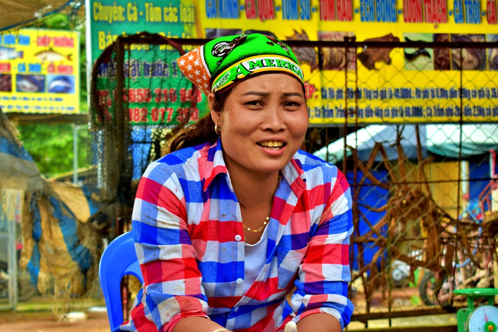 woman in white, red, and blue plaid top sitting beside linked fence