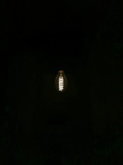 A glowing light bulb is suspended in complete darkness, with its intricate filament clearly visible.