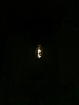 A glowing light bulb is suspended in complete darkness, with its intricate filament clearly visible.