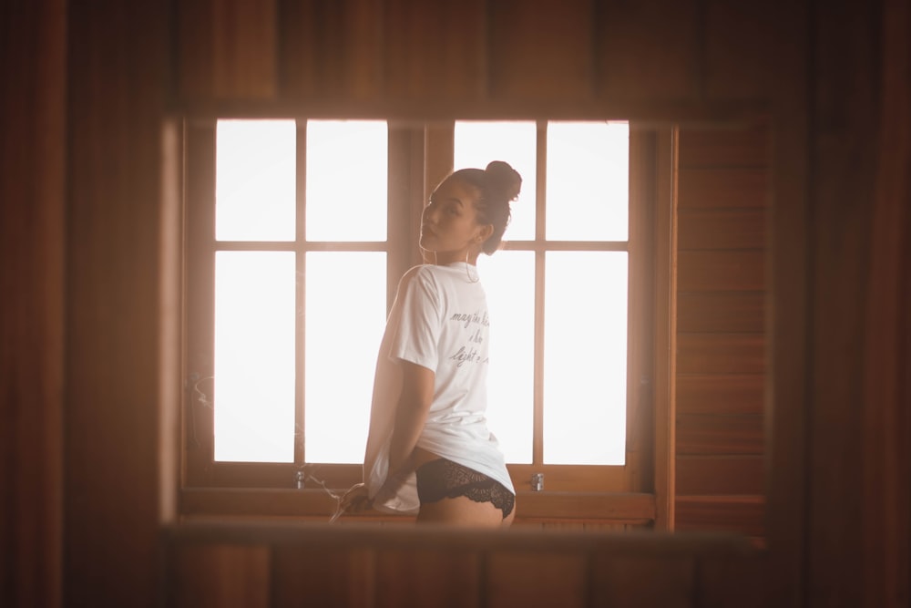 Frau trägt weißes T-Shirt vor dem Fenster