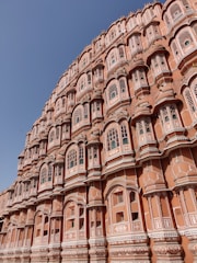 An intricately designed architectural structure with numerous small windows and detailed latticework. The building has a distinct pinkish hue and showcases traditional Indian design elements.