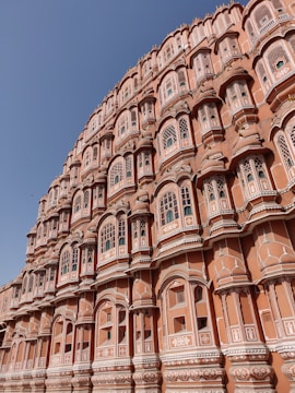An intricately designed architectural structure with numerous small windows and detailed latticework. The building has a distinct pinkish hue and showcases traditional Indian design elements.
