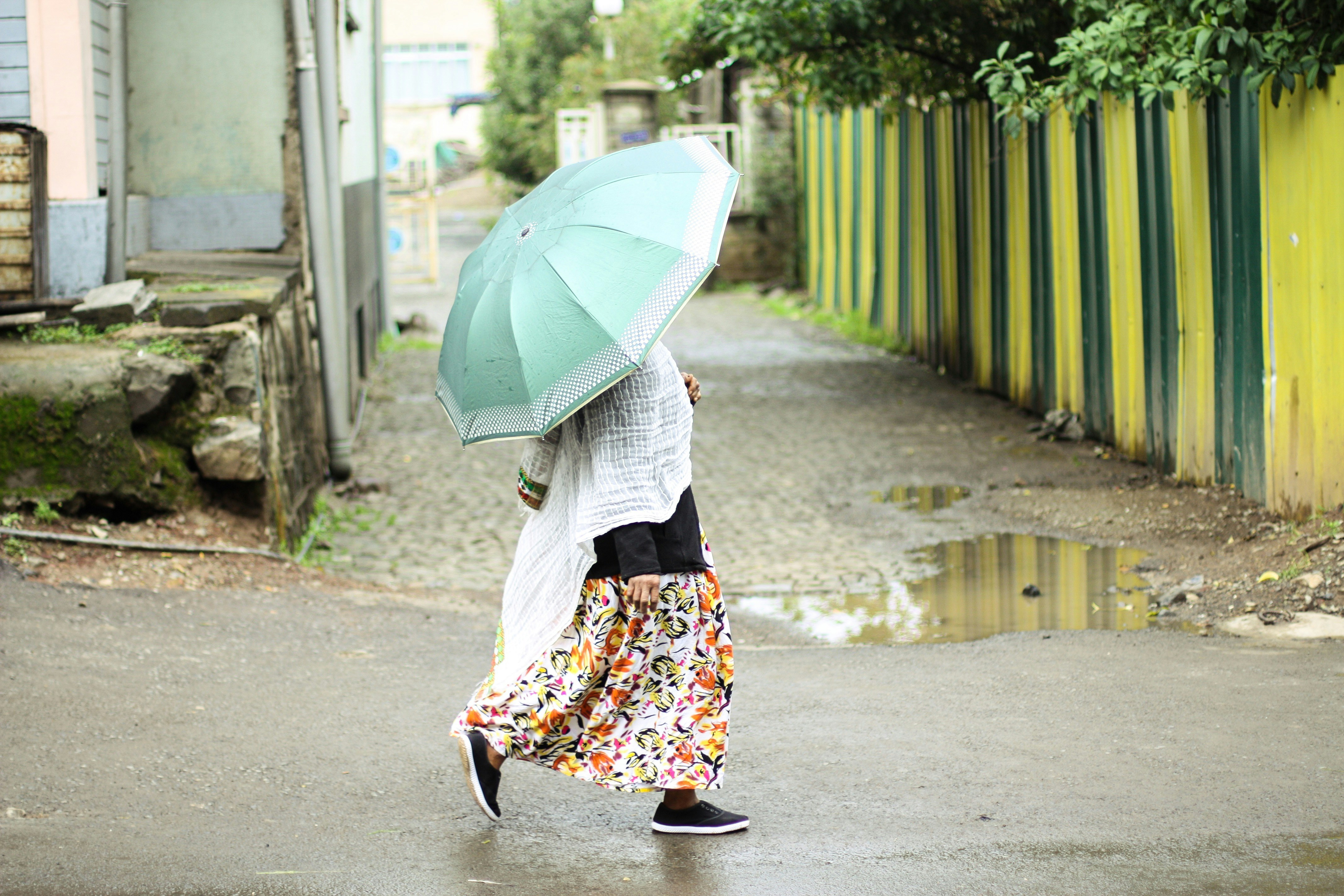 woman walking on street holding teal umbrella