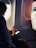 A person is seated next to an airplane window, looking at a smartphone. The natural light from the window illuminates the person's face and hand. The seat-back pocket in front of them contains safety information cards.