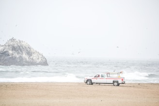 A pickup truck driving along a coastal road with waves crashing beside it.