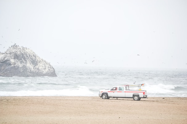 A pickup truck driving along a coastal road with waves crashing beside it.