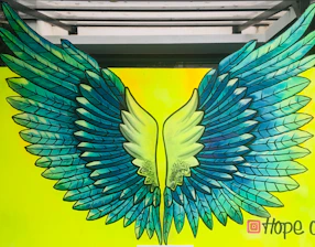 Children painting colorful wings on a large mural together outdoors.