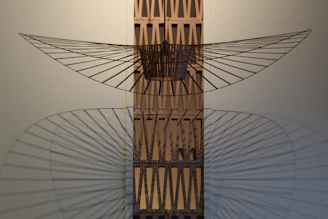 Abstract sculpture made of metal and wood, casting dynamic shadows on a white wall.