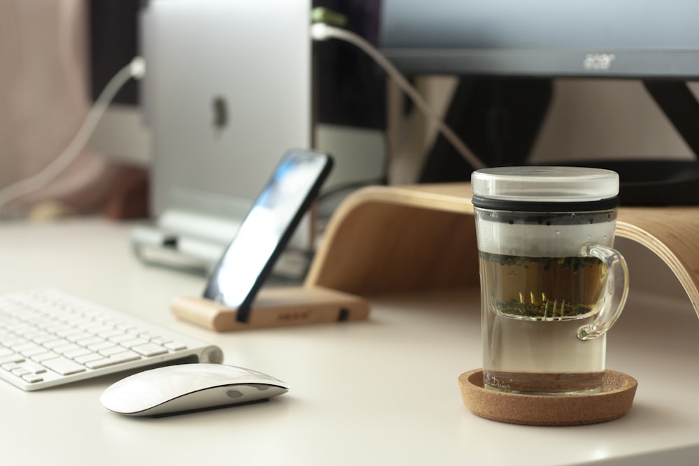 clear glass mug beside Apple Magic Mouse