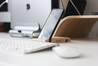 A sleek desktop folding phone holder displaying a smartphone at a comfortable viewing angle on a wooden desk.