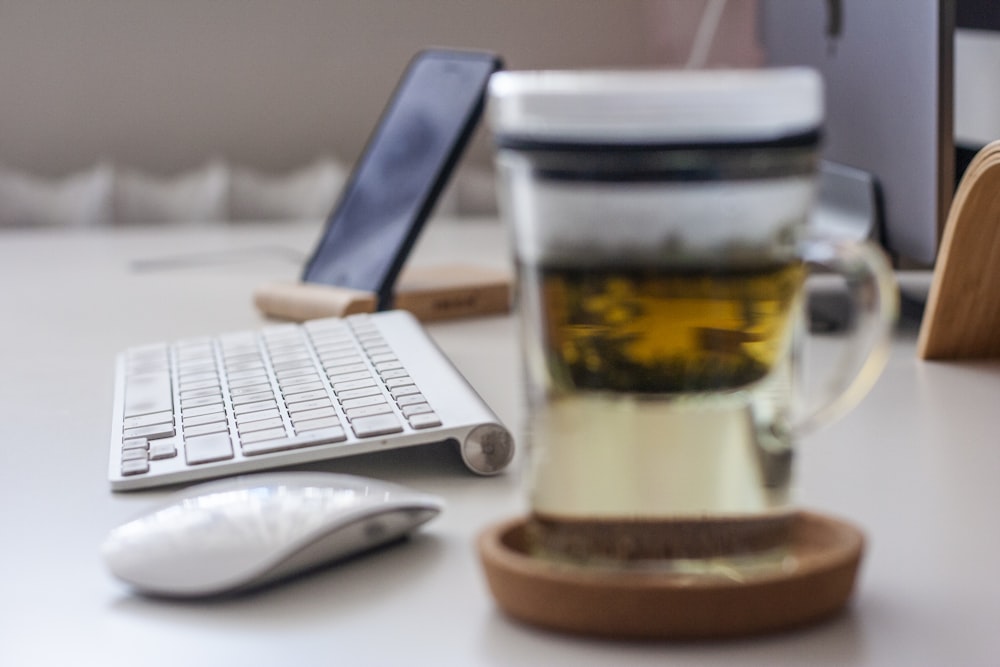 clear glass cup on round drink coaster beside Apple Magic Mouse and wireless keyboard