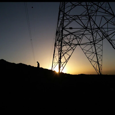 Technician monitoring AI-powered condition sensors on a power grid tower at sunset.