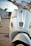 Close-up view of a white scooter parked on the side of a road. The scooter has a number plate with the registration MH 12 QX 6622. The background shows a blurred urban environment with the hint of parked cars and a building.