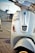 Close-up view of a white scooter parked on the side of a road. The scooter has a number plate with the registration MH 12 QX 6622. The background shows a blurred urban environment with the hint of parked cars and a building.
