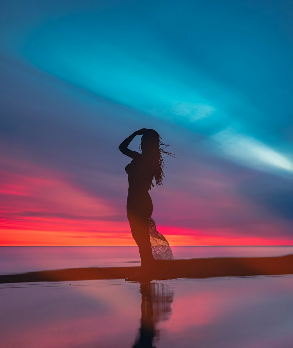 a woman standing on a beach at sunset