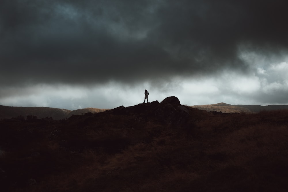 person standing on cliff under nimbus clouds